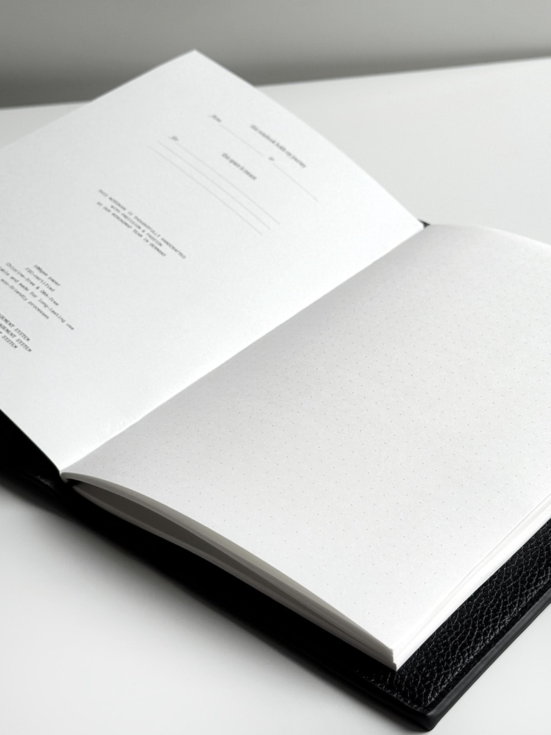 K&ouml;nnte beinhalten: Ein offenes schwarzes Notizbuch mit wei&szlig;en Punktrasterseiten. Die linke Seite hat Linien f&uuml;r das Datum und andere Informationen. Die rechte Seite ist leer mit einem Punktrastermuster.