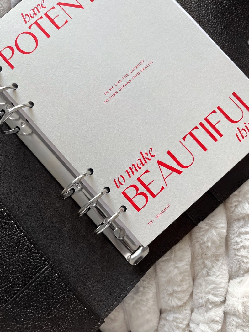 Może przedstawiać: Otwarty planer z białymi stronami i czerwonym tekstem. Tekst brzmi "have POTENTIAL" i "to make BEAUTIFUL things." Dodatkowy tekst brzmi "IN ME LIES THE CAPACITY TO TURN DREAMS INTO REALITY" i "MY ROADMAP."