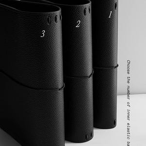 May include: Three black leather journal covers with white numbers 1, 2, and 3. Each cover has a textured surface and a black elastic band. The text on the right says "Choose the number of inner elastic bands."