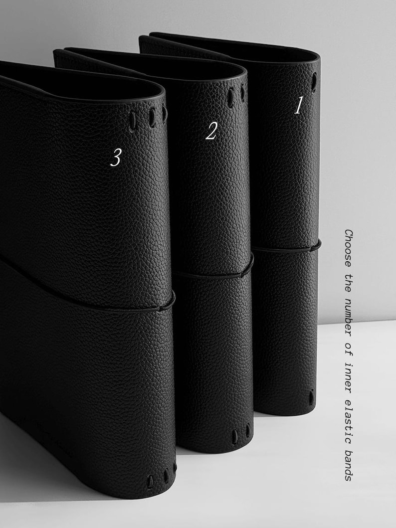 May include: Three black leather journal covers with white numbers 1, 2, and 3. Each cover has a textured surface and a black elastic band. The text on the right says "Choose the number of inner elastic bands."