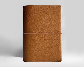May include: A brown leather journal with a textured surface. The journal is secured with a matching elastic band. The cover is rectangular with rounded edges. The journal is approximately 20 cm tall and 13 cm wide.