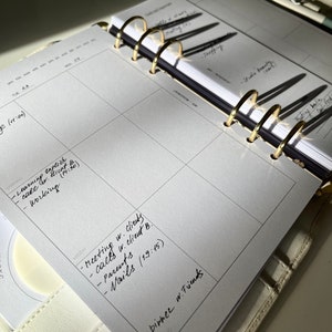 May include: Open planner with gold rings, featuring a weekly calendar layout. The pages are filled with handwritten notes, including appointments and to-do lists. The planner is open to a week view, with the days of the week visible.