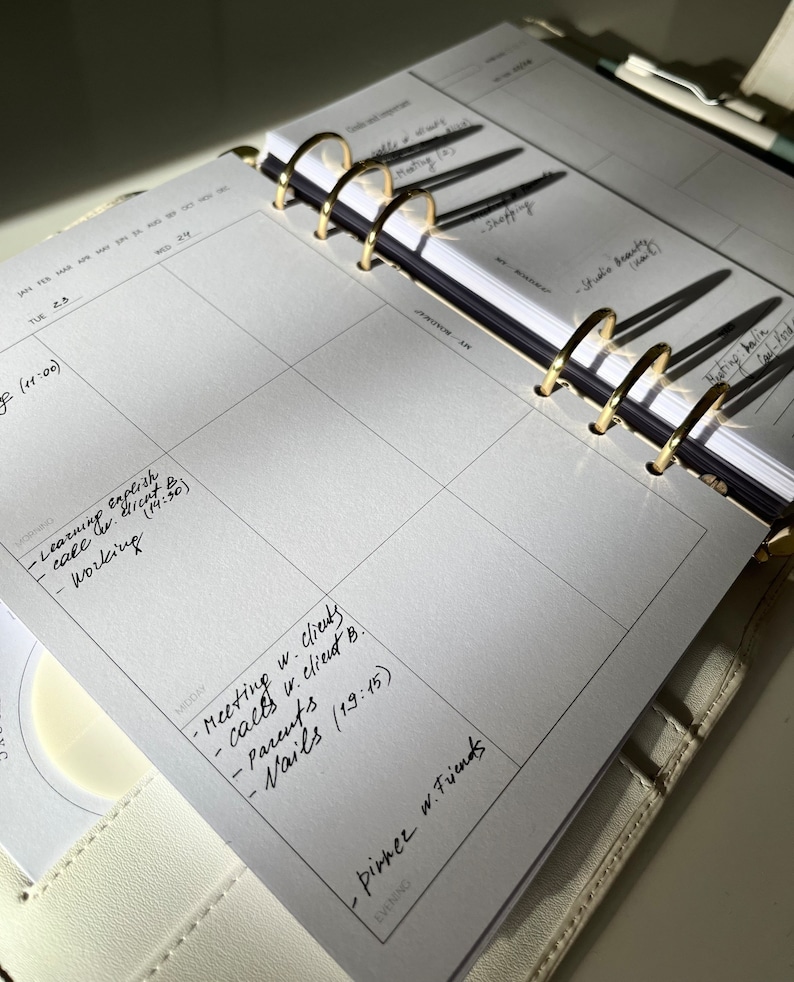 May include: Open planner with gold rings, featuring a weekly calendar layout. The pages are filled with handwritten notes, including appointments and to-do lists. The planner is open to a week view, with the days of the week visible.