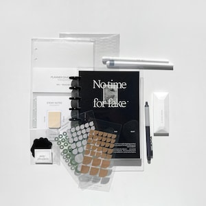 May include: A black planner with the text "No time for fake" on the cover. The planner is open to reveal a clear plastic pocket with a variety of stickers and a sticky note pad. The planner also includes a clear plastic divider with the text "Planner Dividers" and a clear plastic pocket with the text "Sticky Notes".