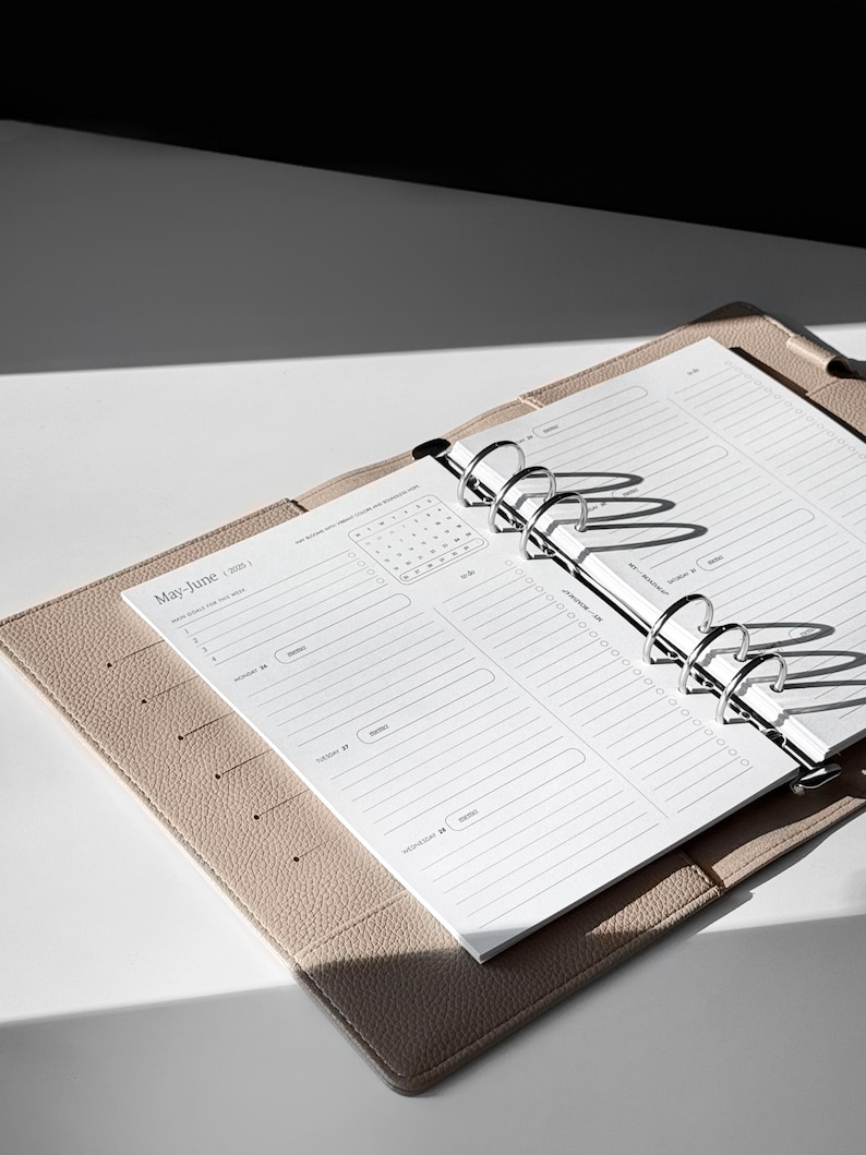 May include: A beige leather bound planner with silver rings and a white page open to the May-June 2020 calendar section. The page has a monthly calendar and a daily planner section with lines for writing.