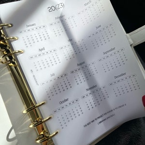 Pu&ograve; includere: Una pagina di agenda bianca con un calendario 2023 da gennaio a dicembre, anelli di rilegatura in metallo dorato sul lato sinistro, il testo MY-ROADMAP e la citazione THE BEST WAY TO PREDICT THE FUTURE IS TO CREATE IT (ABRAHAM LINCOLN).