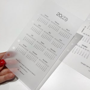 Pu&ograve; includere: Un inserto per agenda traslucido e satinato con una panoramica del calendario 2023. La pagina include dodici griglie mensili, il testo 20(23), la citazione THE BEST WAY TO PREDICT THE FUTURE IS TO CREATE IT (ABRAHAM LINCOLN) e MY-ROADMAP.
