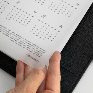 May include: A black leather planner containing a white calendar insert with months from August to December. The page features a printed quote about personal growth and the text MyRoadmap in parentheses at the bottom of the translucent sheet.