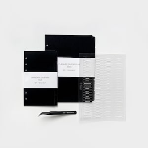 以下が含まれることがあります： 「MY-ROADMAP」と「PLANNER DIVIDERS A5 black」と「PERSONAL DIVIDERS black」のテキストが書かれた黒いプランナー用仕切りとパーソナル仕切り。 「NOTES」、「APPOINTMENTS」、「BUDGET」、「GOALS」、「CONTACTS」とラベル付けされたタブが付いた透明なプラスチックシートと、黒いピンセット。