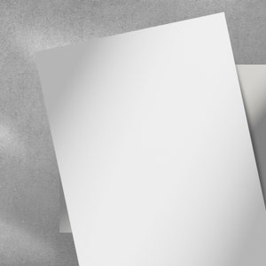May include: A close-up shot of two white sheets of paper, slightly angled, against a gray textured background. The paper is bright white, and the lighting creates subtle shadows. The image suggests a clean, minimalist aesthetic, suitable for stationery or print design.