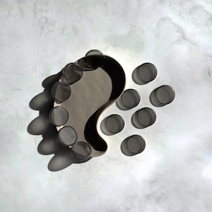 May include: A grey ceramic tray shaped like a teardrop with a raised edge. The tray is filled with ten small, clear glass cups.