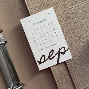 May include: A white rectangular calendar card for September 2027 with the text Return to Yourself and sep written in large black script. The calendar displays days of the week and dates, with the number 13 circled and the text Happy Birthday, MyRoadmap!