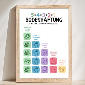 May include: A framed print with the German text "5-4-3-2-1 BODENHAFTUNG" in colorful text. The print features illustrations of eyes, hands, ears, noses, and a mouth, with corresponding numbered prompts for sensory awareness.