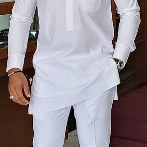 May include: A white long-sleeved shirt with a mandarin collar and a small pocket on the left chest. The shirt is paired with white pants.