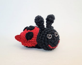 May include: A crocheted ladybug toy with black and red accents. The ladybug has black eyes and a smiling mouth.