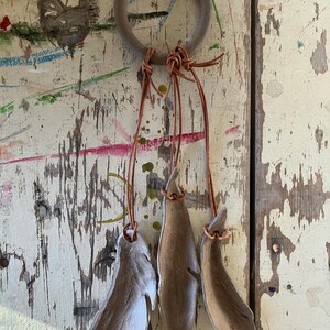 May include: A wooden ring with brown leather cords and three brown clay feathers hanging from it.