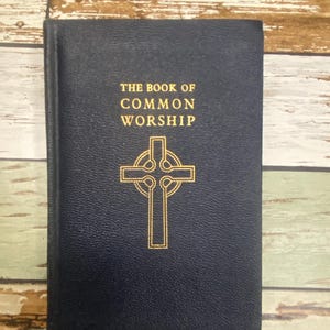 Peut inclure: Un livre bleu marine intitulé "The Book of Common Worship" avec des lettres dorées et une croix dorée. Le livre a une couverture bleu foncé et un signet en ruban.