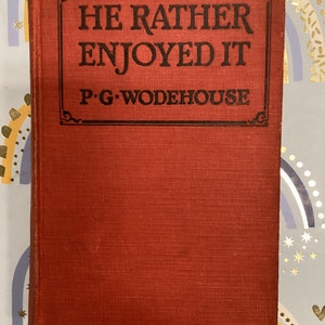 May include: A red hardcover book with the title "He Rather Enjoyed It" and the author "P.G. Wodehouse" printed in black on the front cover.
