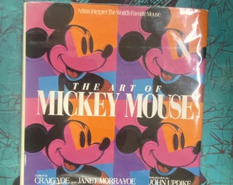 May include: A book titled "The Art of Mickey Mouse" with a pop art style cover. The cover features four images of Mickey Mouse with pink, orange, and purple backgrounds. The book is edited by Craig Yoe and Janet Morra-Yoe, with an introduction by John Updike.