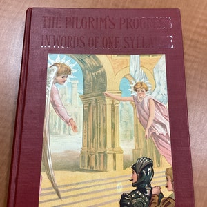 Op de afbeelding: Een rood boek met de titel "The Pilgrim's Progress in Words of One Syllable" op de omslag. De omslag toont een illustratie van twee engelen met vleugels, een ridder in harnas en een jong persoon.