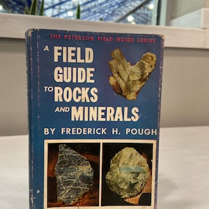 May include: A blue book titled "A Field Guide to Rocks and Minerals" by Frederick H. Pough. The book cover features a photo of a rock formation and the text "3rd edition, with 72 new color illustrations 264 photographs, 149 in full color."