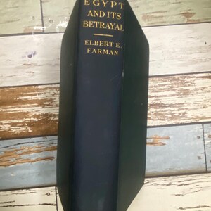 Pode incluir: Um livro de capa dura intitulado "Egypt and Its Betrayal" de Elbert E. Farman. O livro tem uma capa azul escura com letras douradas. O nome da editora, Grafton, está na parte inferior. O livro está em bom estado.