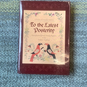 May include: A hardcover book titled "To the Latest Posterity" with a burgundy cover. The cover features a decorative design with two birds, floral accents, and the text "Pennsylvania-German Family Registers in the Fraktur Tradition."