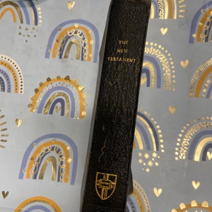 May include: A black leather-bound book with gold lettering that reads "The New Testament".