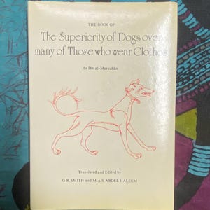 May include: A vintage book titled "The Superiority of Dogs over many of Those who wear Clothes" with a red illustration of a dog. The book's cover is off-white with black text and the author's name. The book is translated and edited by G.R. Smith and M.A.S. Abdel Haleem.