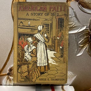 May include: A vintage book titled "American Patty: A Story of 1812" by Adele E. Thompson. The cover features an illustration of two women in period clothing, one spinning yarn on a spinning wheel, the other standing in a doorway.