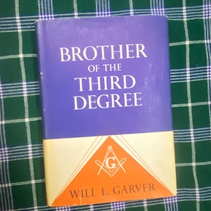 Könnte beinhalten: Ein Buch mit dem Titel Brother of the Third Degree von Will L. Garver. Der Einband zeigt einen violetten oberen Bereich mit weißem Text und einen unteren orangefarbenen dreieckigen Bereich mit einem weißen Winkel- und Zirkelsymbol und dem Buchstaben G.