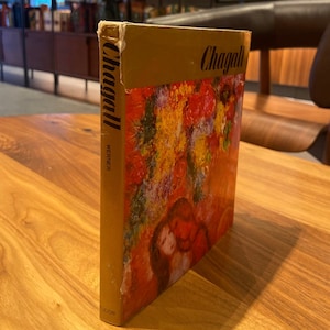 May include: A gold-colored book with the title "Chagall" printed in black on the cover. The cover features a painting of a couple embracing, surrounded by colorful flowers.