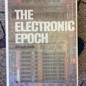 May include: The cover of a book titled "The Electronic Epoch" by Elizabeth Antébi. The cover features a detailed illustration of a computer chip.