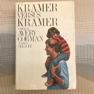 Könnte beinhalten: Ein Vintage-Taschenbuch mit dem Titel "Kramer gegen Kramer" von Avery Corman. Das Cover zeigt eine Illustration eines Mannes, der ein Kind auf seinen Schultern trägt. Das Kind trägt ein rot-blau gestreiftes Hemd. Das Buch ist vor einem neutralen Hintergrund.