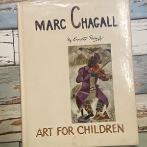 May include: A book titled "Marc Chagall" by Ernest Raboff. The cover features a colorful illustration of a figure playing a violin. The title "Art for Children" is printed at the bottom of the cover.
