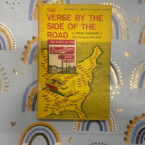 Peut inclure: Un livre vintage intitulé "The Verse by the Side of the Road" par Frank Rowsome, Jr. La couverture jaune du livre présente une carte des États-Unis et une illustration d'un panneau Burma-Shave. Le livre est une collection de rimes de bord de route.