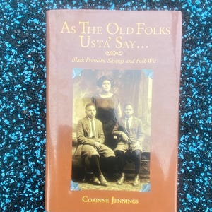 May include: A brown book titled As The Old Folks Usta' Say... Black Proverbs, Sayings and Folk-Wit by Corinne Jennings. The cover features a sepia-toned photograph of a woman standing behind two seated boys wearing suits and ties.