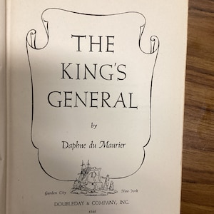 以下が含まれることがあります： ダフネ・デュ・モーリア著「THE KING'S GENERAL」のタイトルが書かれた開いた本のページ。タイトルは太字のセリフ体で、装飾的なフレーム内にあります。「DOUBLEDAY & COMPANY, INC.」と年号「1946」を含む出版社の情報も表示されています。