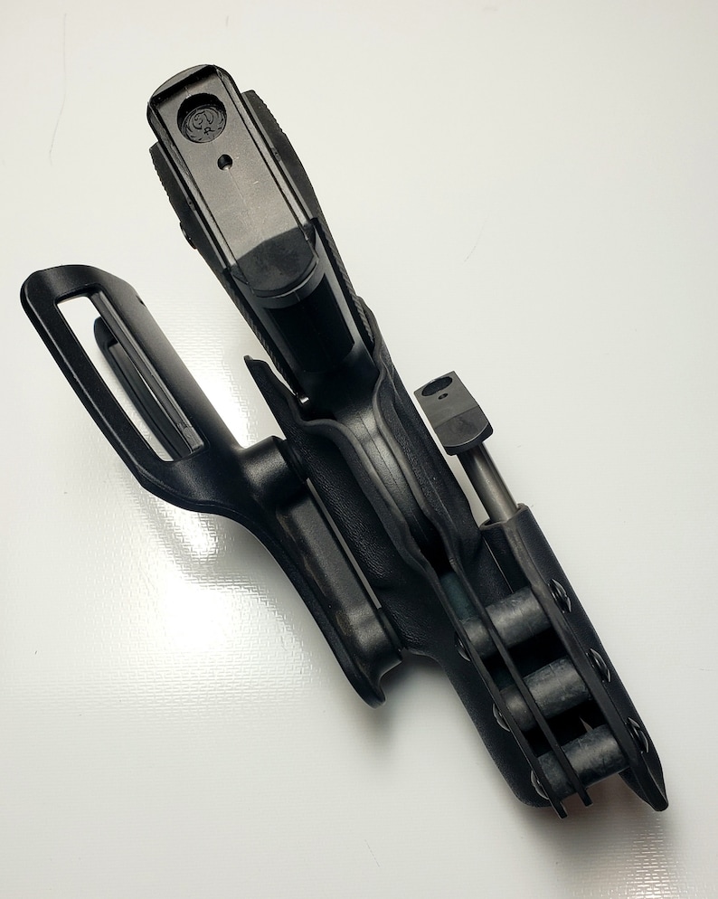 K&ouml;nnte beinhalten: Schwarze Polymer-Pistolenholster mit G&uuml;rtelschlaufe und Magazinhalter. Das Holster ist so konzipiert, dass es eine Schusswaffe sicher h&auml;lt. Das Design umfasst ein R&uuml;ckhaltesystem und besteht aus strapazierf&auml;higem, geformtem Kunststoff.