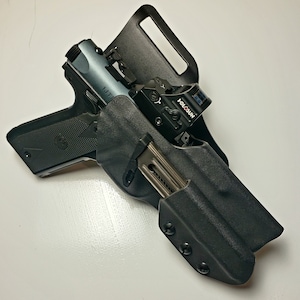 K&ouml;nnte beinhalten: Eine schwarze Polymerholster mit einer halbautomatischen Pistole und einem Magazin. Die Pistole hat einen grauen Schlitten und ein Rotpunktvisier. Die Holster ist f&uuml;r das Tragen am G&uuml;rtel konzipiert.
