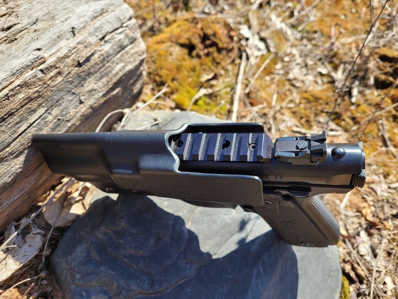 May include: A black handgun with a black holster. The handgun has a black polymer frame and a black metal slide. The slide has a black polymer sight and a black metal rail on top. The holster is made of black polymer and has a black polymer belt loop.