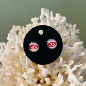 May include: A pair of silver stud earrings with a white background and a red "B" logo.
