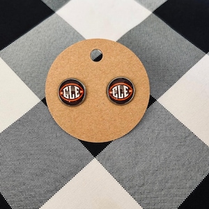 May include: A pair of silver stud earrings with a brown and orange football design featuring the text "CLE".