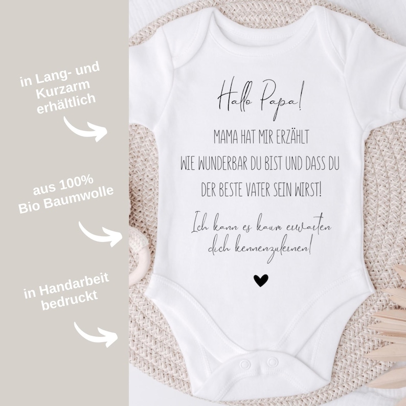 May include: White baby onesie with black text that reads "Hallo Papa! Mama hat mir erz&auml;hlt wie wunderbar du bist und dass du der beste Vater sein wirst! Ich kann es kaum erwarten dich kennenzulernen!"  The onesie is available in long and short sleeves and is made from 100% organic cotton.