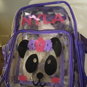 May include: Purple clear plastic backpack with a panda face design and the name "NYLA" printed on the front.