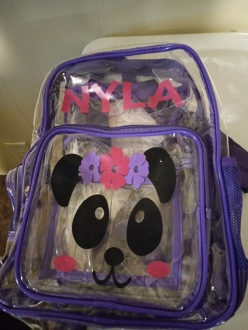May include: Purple clear plastic backpack with a panda face design and the name "NYLA" printed on the front.