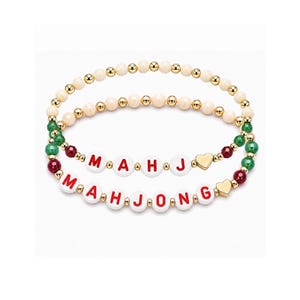 May include: Two beaded bracelets featuring small gold-tone spacer beads. One bracelet has cream-colored beads, while the other features green and red faceted beads with white letter beads spelling MAHJONG and a small gold-tone heart charm.