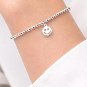 May include: A white ceramic mug with a black handle and the text "But First, Coffee" in a bold, black font. The mug is set against a blurred background, suggesting a cozy setting. The mug appears to be approximately 4 inches tall.