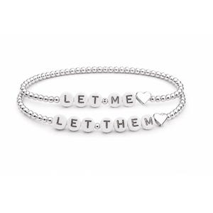 May include: Two silver-toned beaded stretch bracelets. The top bracelet features white round beads spelling LET ME and a silver heart charm. The bottom bracelet features white round beads spelling LET THEM and a silver heart charm.