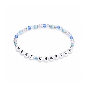 May include: A beaded bracelet with the words "NEXT CHAPTER" spelled out in white letter beads. The bracelet features clear and blue beads, creating a delicate and stylish accessory.
